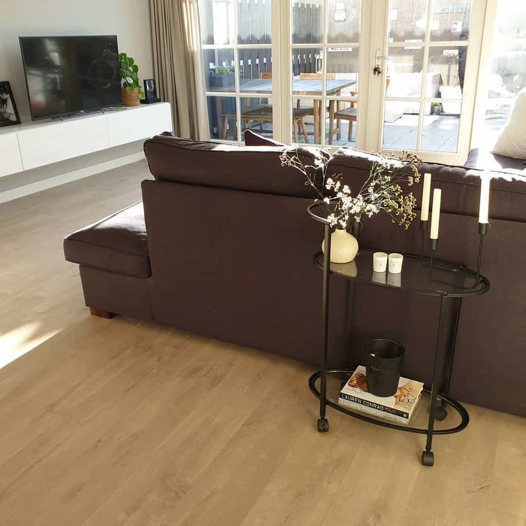 Small black bar cart with vase, candles, and books beside a dark sofa in a modern living room.