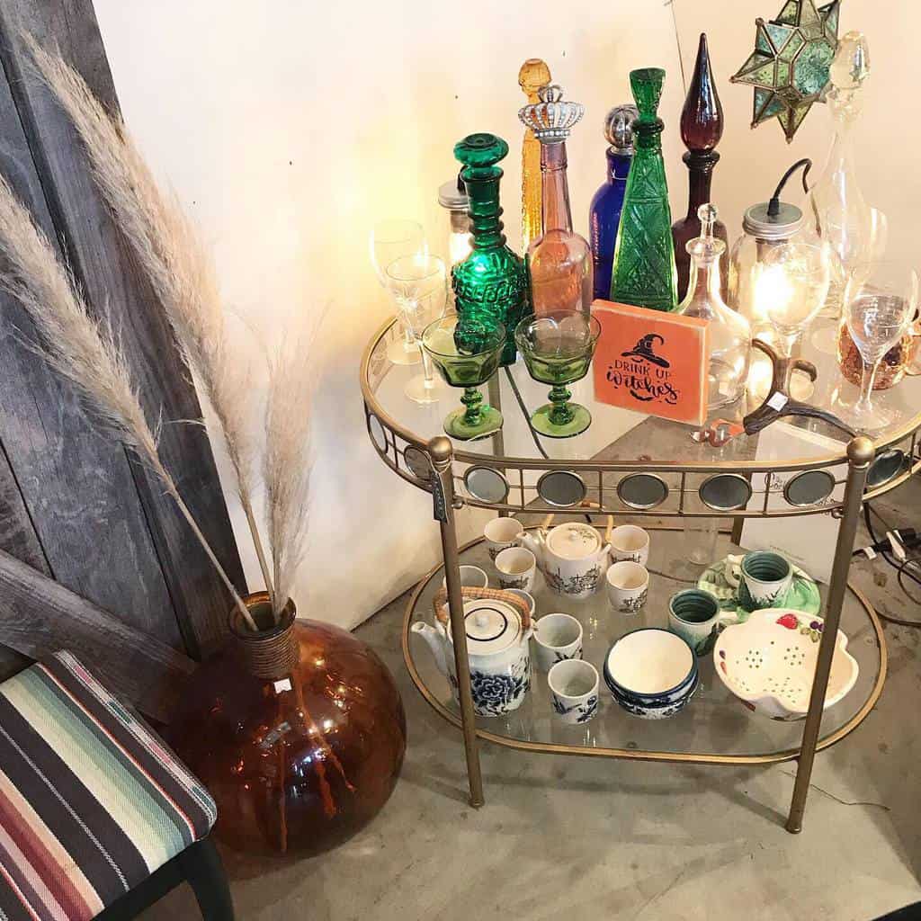 Small gold bar cart with vintage glass bottles, teacups, and decorative lighting elements.