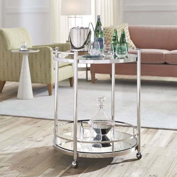 Small silver bar cart with decanter, ice bucket, and sparkling water bottles in a modern living room.