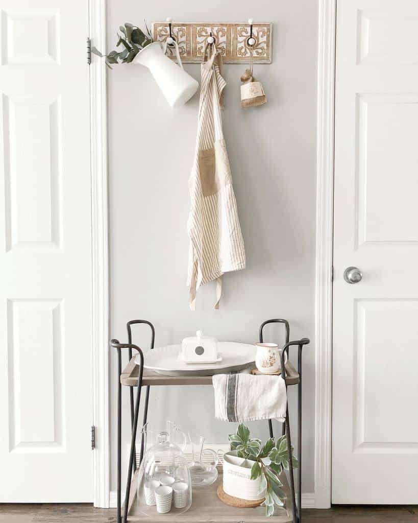 Small bar cart with white dishes, glassware, and a potted plant, hanging apron above.