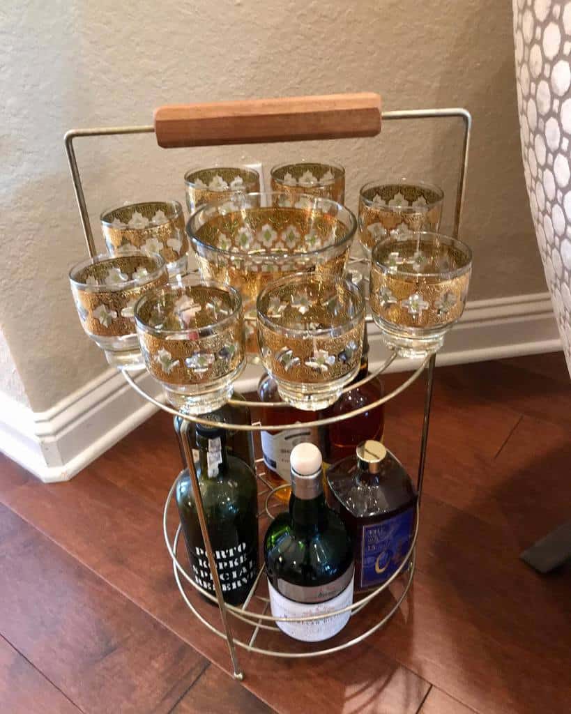 Small steel bar cart with gold-patterned glasses and assorted liquor bottles.