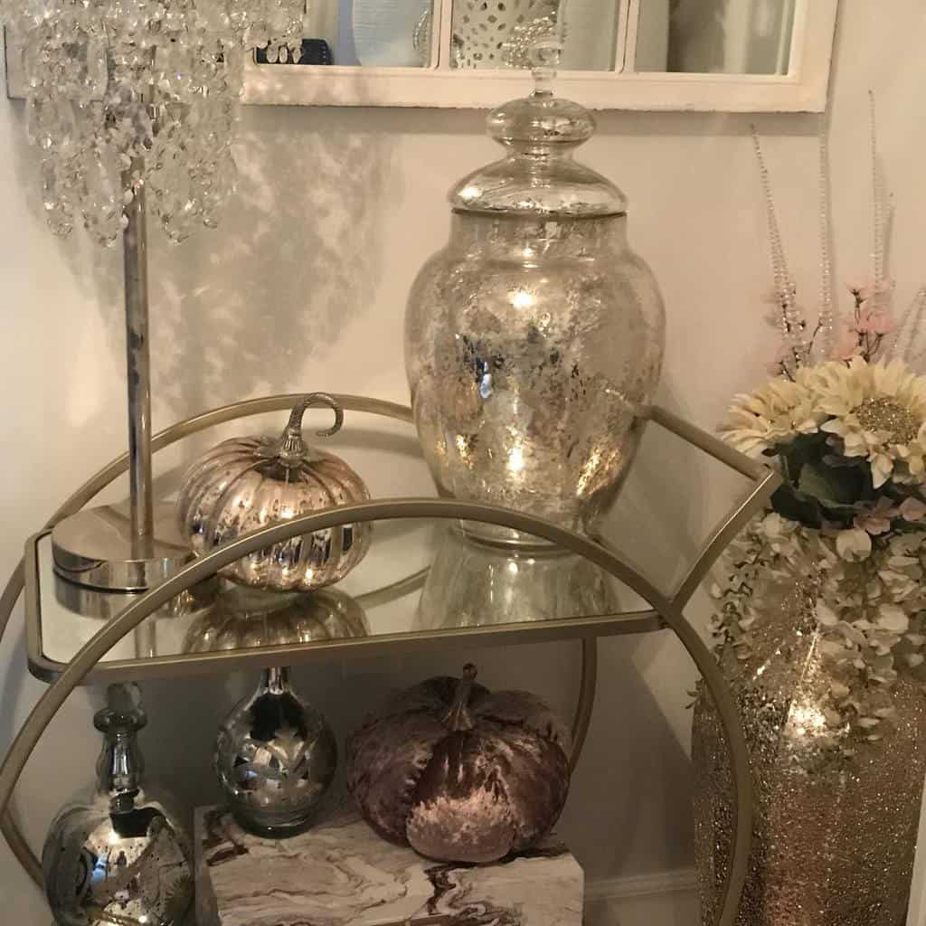 Small bar cart with metallic pumpkins, crystal lamp, and decorative glass jars.