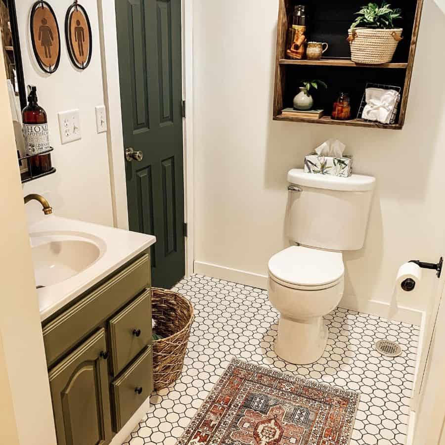 Small country-style bathroom with hexagon tile floor, green vanity, and wooden wall shelf above the toilet.