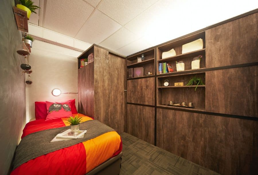 Small bedroom with large brown wardrobe, open shelving, and cozy bedding.