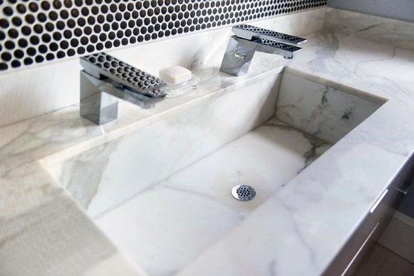 White marble sink with modern faucets and black circular tile backsplash with white grout.