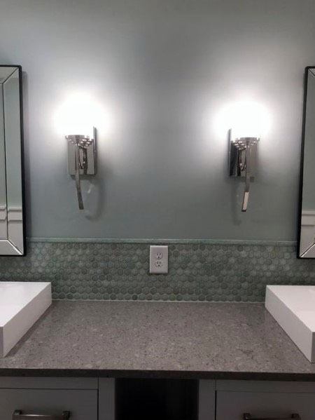 Bathroom vanity with grey countertop, green circular tile backsplash, and wall-mounted lights.