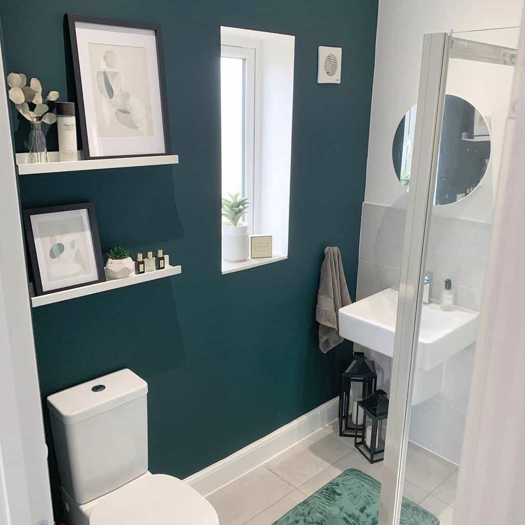 Small bathroom with dark green feature wall, floating shelves, and a compact shower and sink.