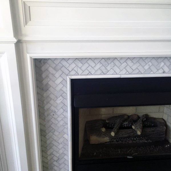 Fireplace with small marble herringbone tiles, black insert, and white wooden trim.