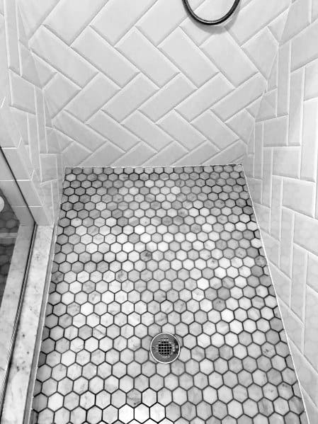 Shower with white herringbone wall tiles and grey hexagonal marble floor tiles.