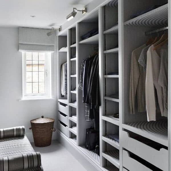 Spacious walk-in closet with grey shelving, neatly hung clothes, and a wicker basket by the window