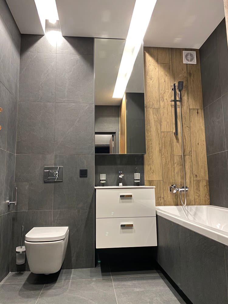 Contemporary bathroom with grey tiles, wood accent wall, floating vanity, and bathtub.