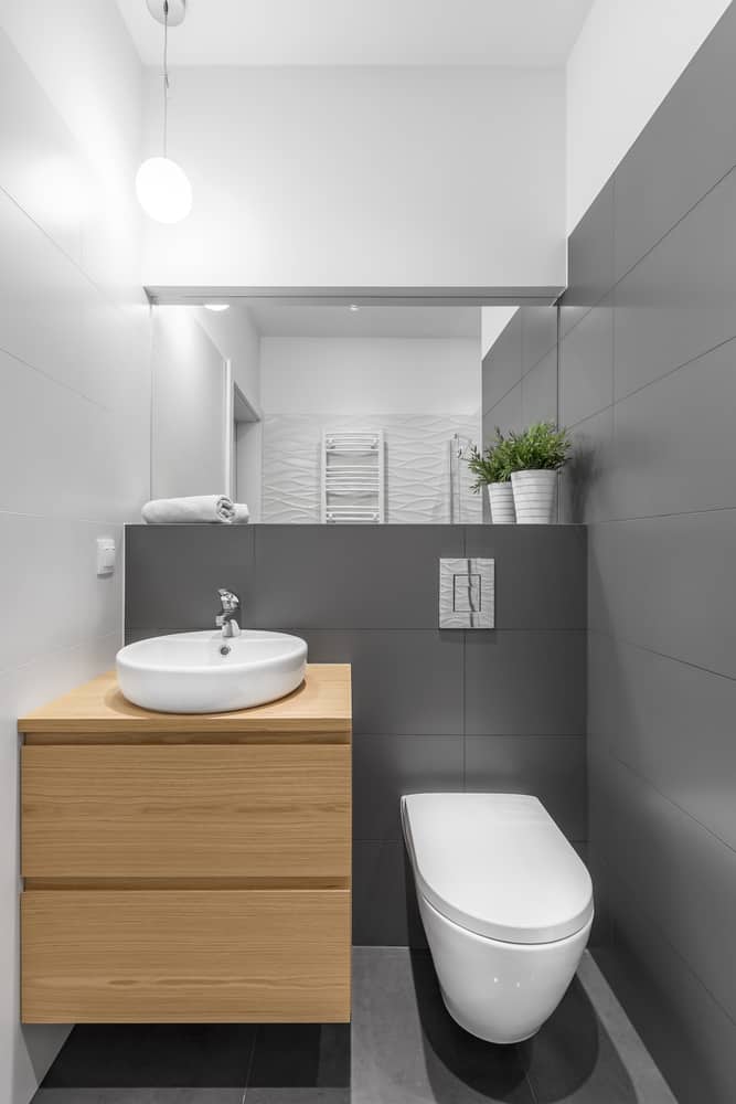 Small modern bathroom with grey tiles, wood vanity, and wall-mounted toilet.