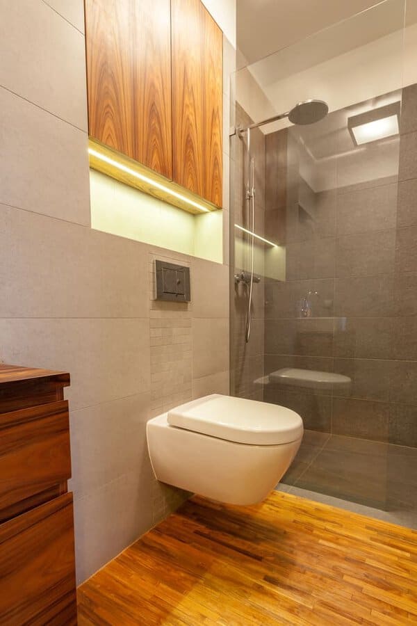 Modern bathroom with wood accents, wall-mounted toilet, and glass-enclosed shower area.