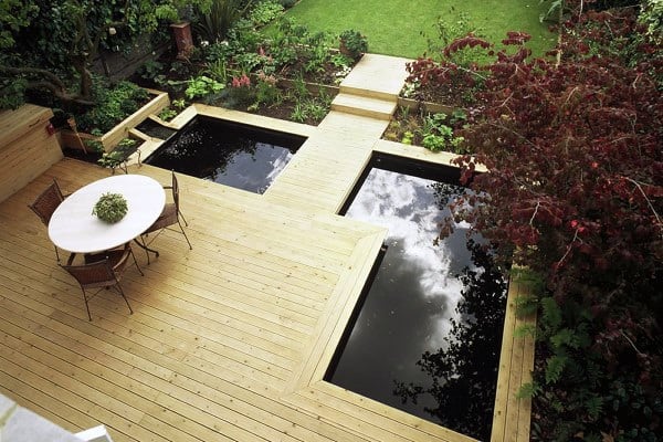 Wooden deck with integrated ponds, surrounded by greenery and featuring an outdoor dining area.