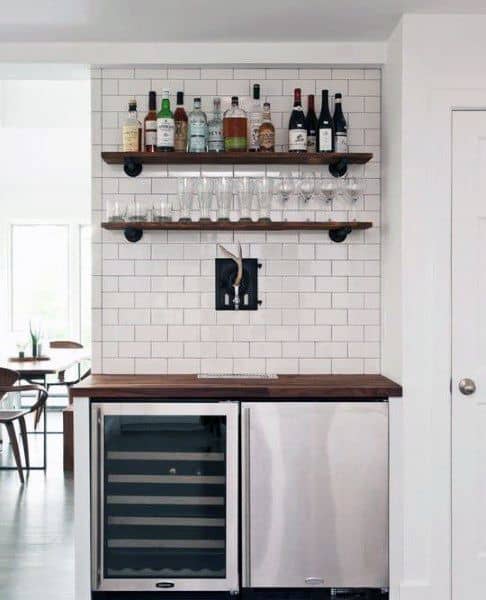 Minimalist mini bar with subway tile backsplash, wood shelves, wine fridge, and beer tap.