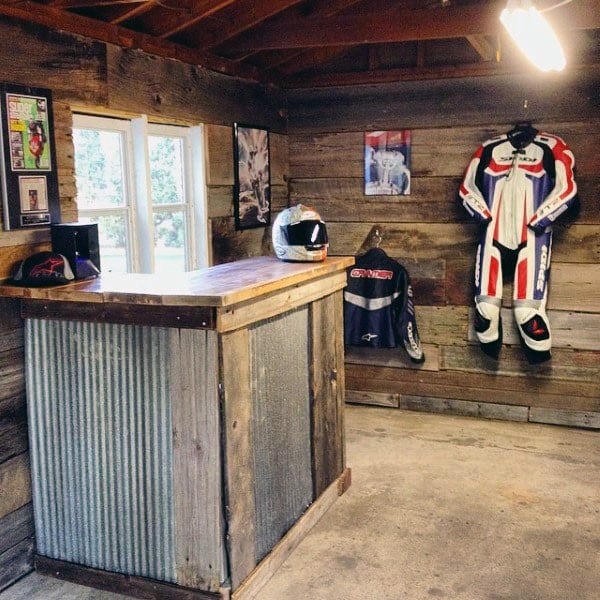 Motorcycle-themed garage bar with corrugated metal paneling, wooden walls, and riding gear decor.