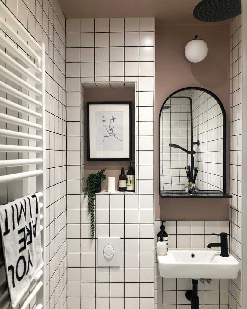 Compact modern bathroom with white grid tiles, wall art, small sink, and black fixtures.