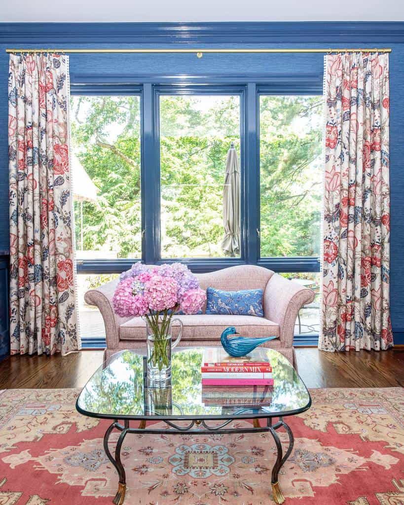 Sunroom with pink sofa, floral curtains, glass coffee table, and vibrant area rug.