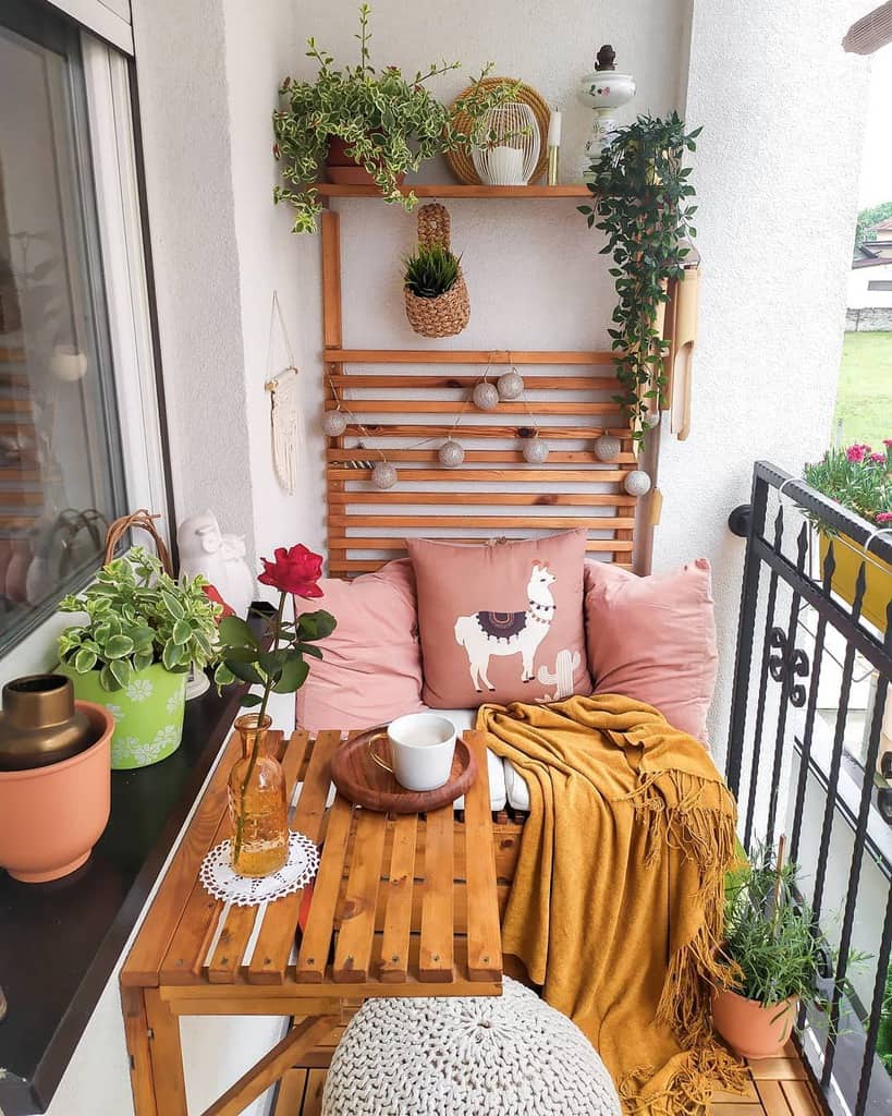 Small cozy balcony with wooden furniture, potted plants, warm textiles, and decorative accents.