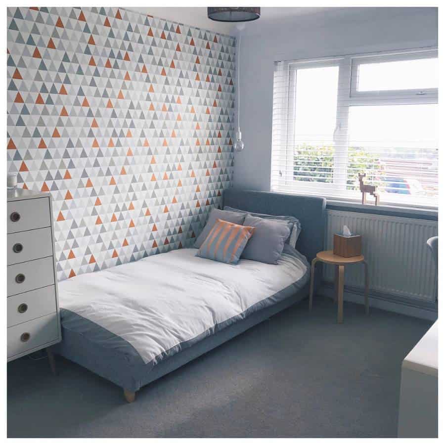 Single bedroom with triangle-patterned wallpaper, cozy bedding, and a minimalist side table.