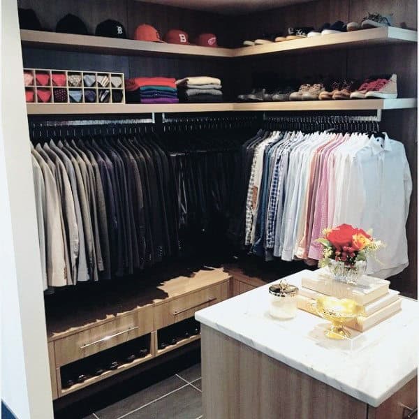 A neatly organized walk-in closet with clothes, hats, shoes, folded items, and a decorated marble-topped island