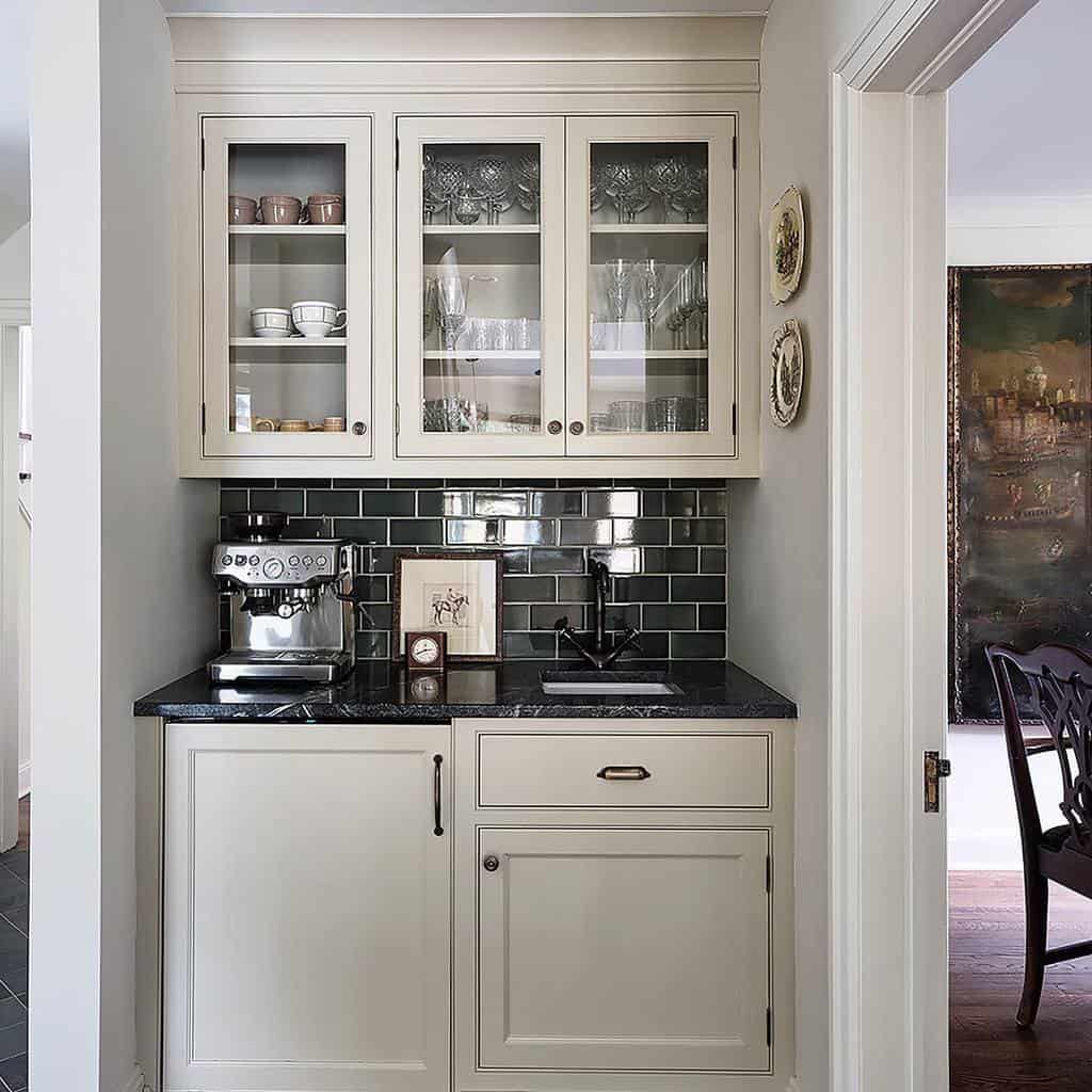 Compact wet bar with glass cabinets, green tile backsplash, and a sleek espresso machine.