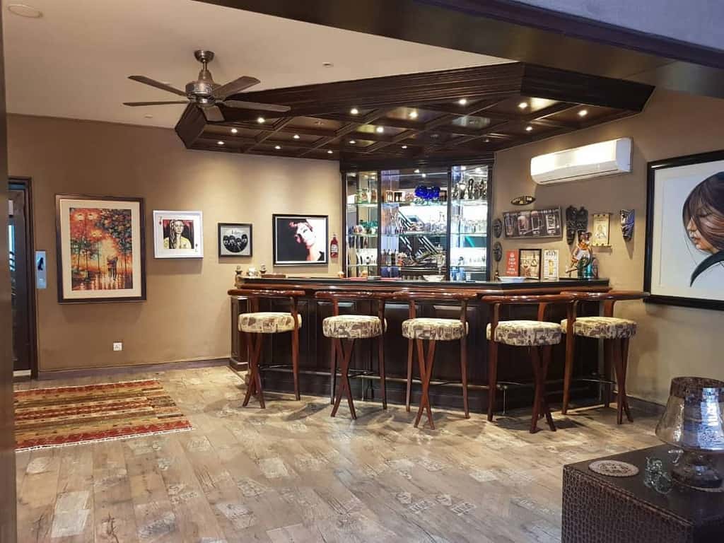 Chic home bar featuring polished wood finishes, upholstered stools, mirrored shelves, and artistic wall decor.