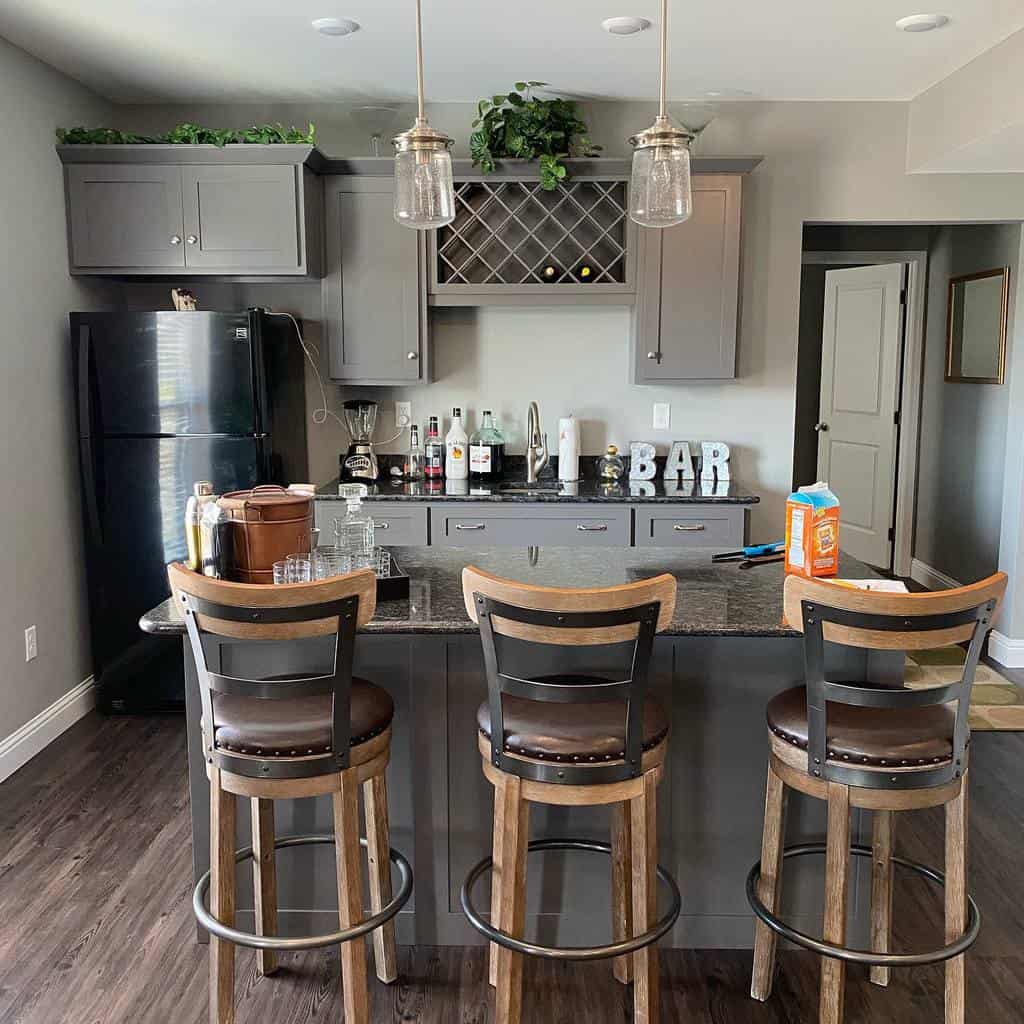 Cozy wet bar with gray cabinetry, a wine rack, rustic barstools, and warm pendant lighting.