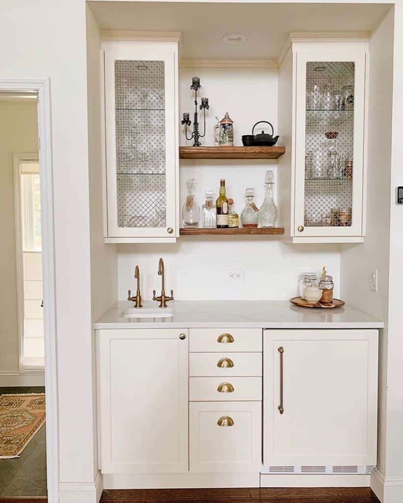 Charming wet bar with cream cabinetry, brass hardware, and rustic wooden shelves for an elegant touch.