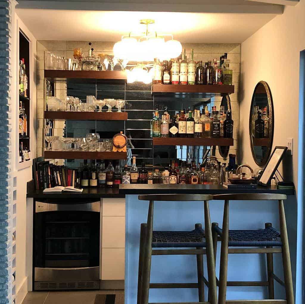 Compact wet bar with mirrored backsplash, floating shelves, and a cozy seating area, perfect for entertaining in style.