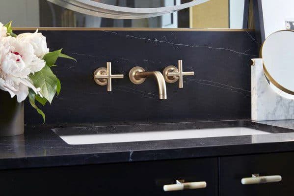 Bathroom with black granite backsplash, gold fixtures, and white countertop sink.