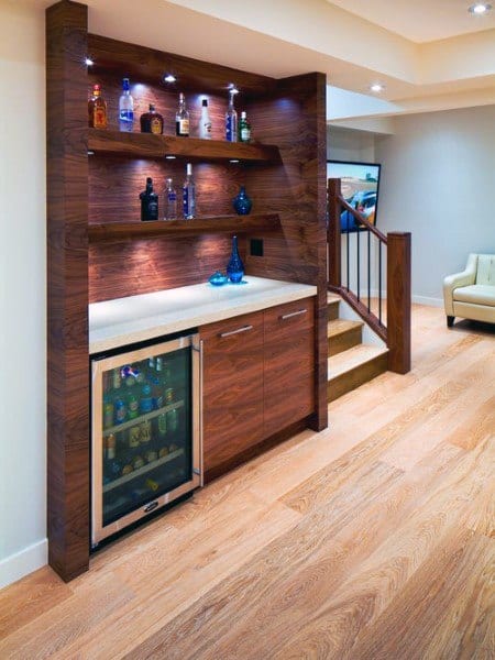 Built-in mini bar with wood shelving, wine fridge, and illuminated display for bottles and decor.