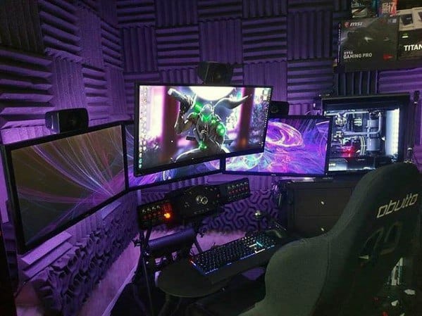 Gaming setup with triple monitors, a keyboard, and PC in a room with purple acoustic panels