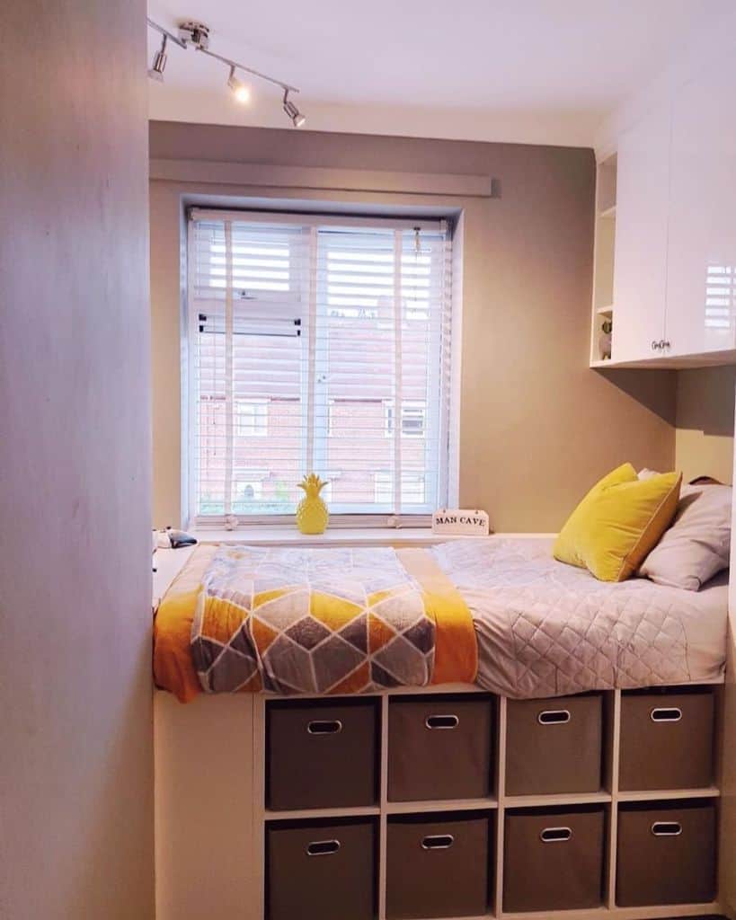 Small bedroom with bed on storage cubes, yellow accents, and large window.