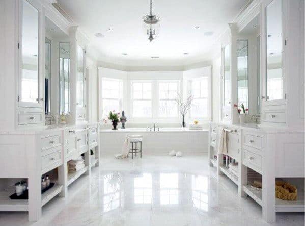 Bright white bathroom with double vanities, large windows, and freestanding bathtub centerpiece.