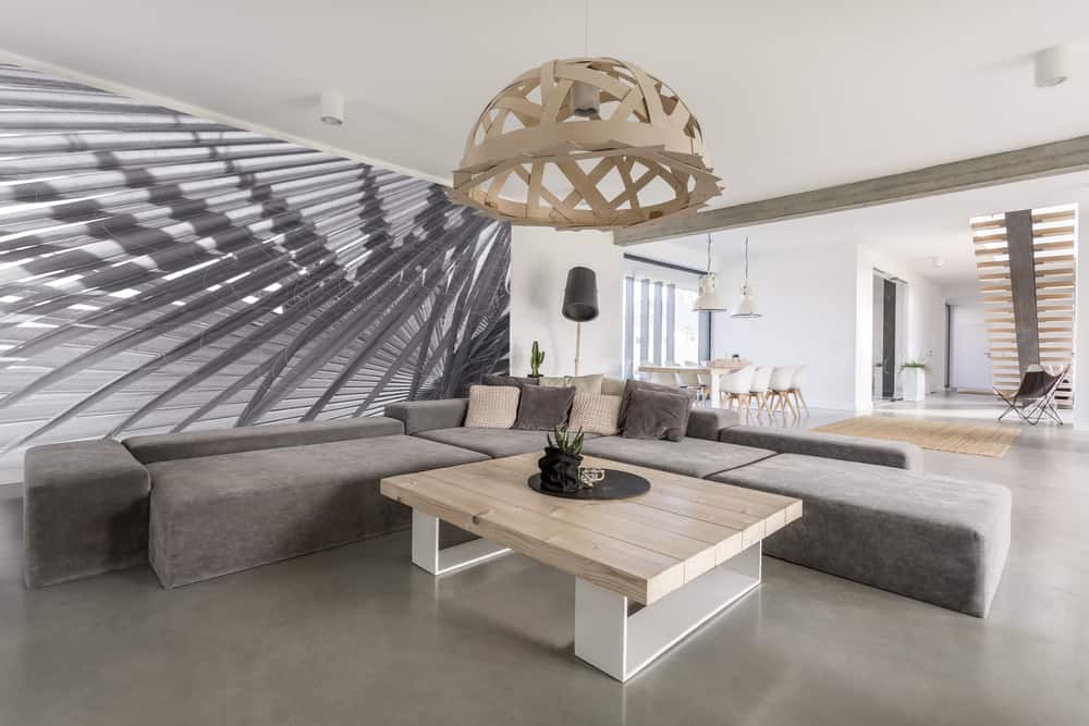 Minimalist living room with a large gray sectional, light wood coffee table, unique statement pendant lamp, and bold abstract wall mural