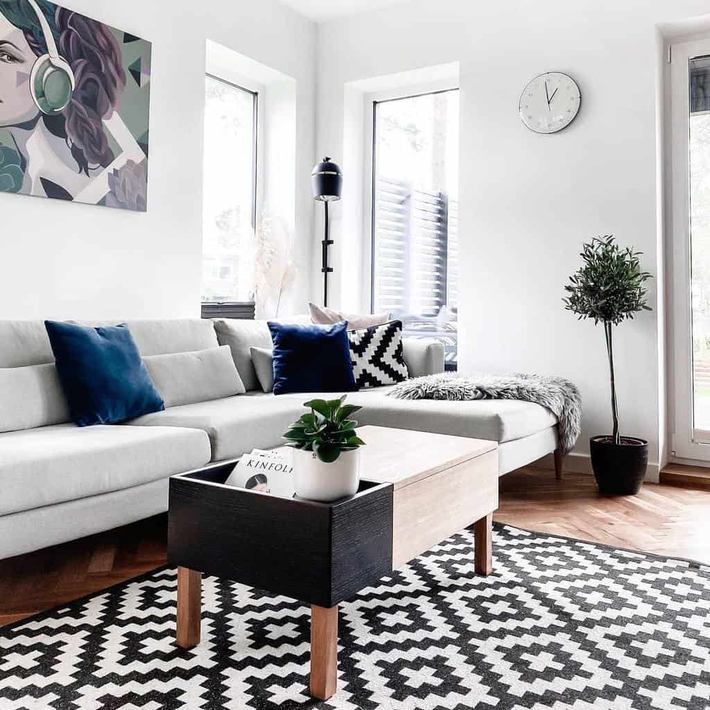 Bright minimalist living room with bold geometric rug, blue accent pillows, modern wall art, and natural light from large windows