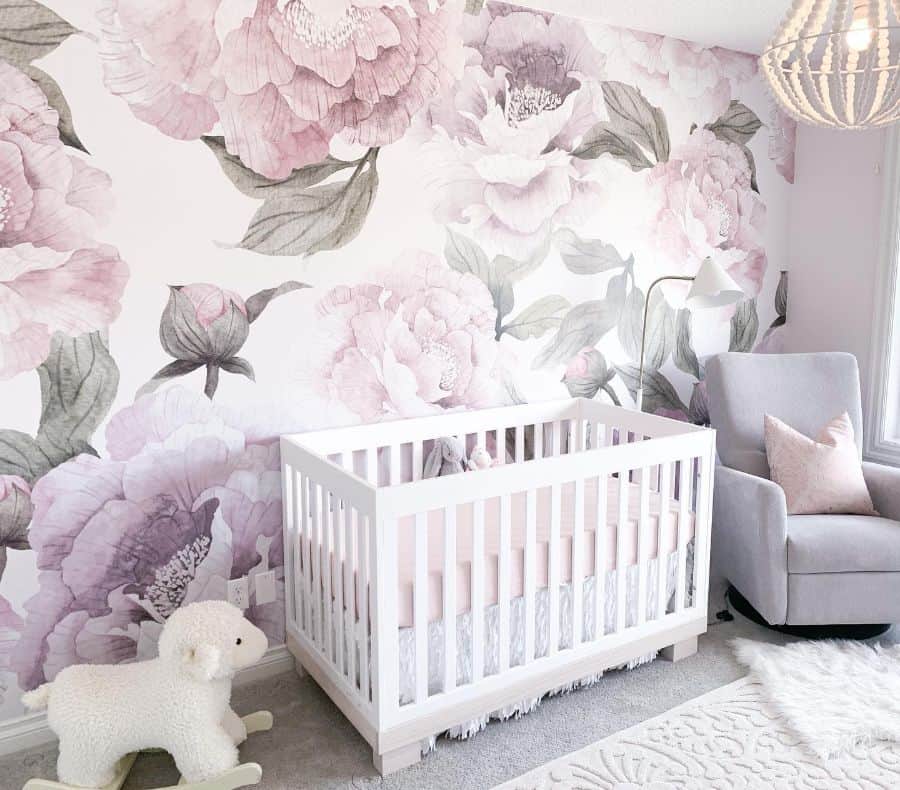 Baby room with large pink floral mural, white crib, gray armchair, and cozy lamb rocker.