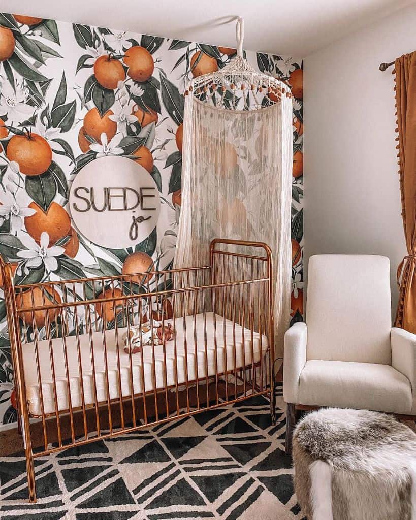 Baby room with copper crib, orange fruit wallpaper, macrame canopy, and geometric rug.