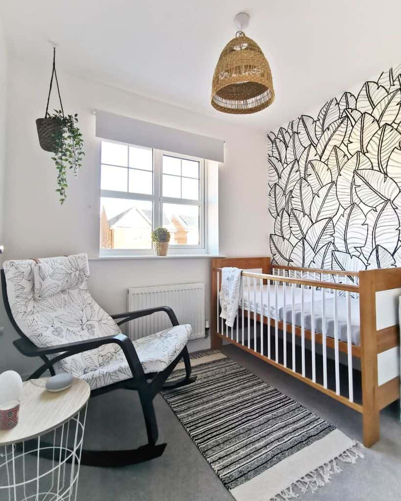 Baby room with leaf-patterned feature wall, wooden crib, rocking chair, and woven decor accents.