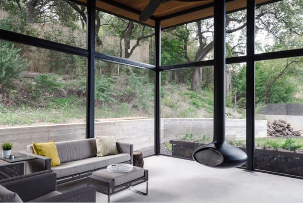 The sunroom features black steel-framed windows, a sleek hanging fireplace, and minimalist seating.