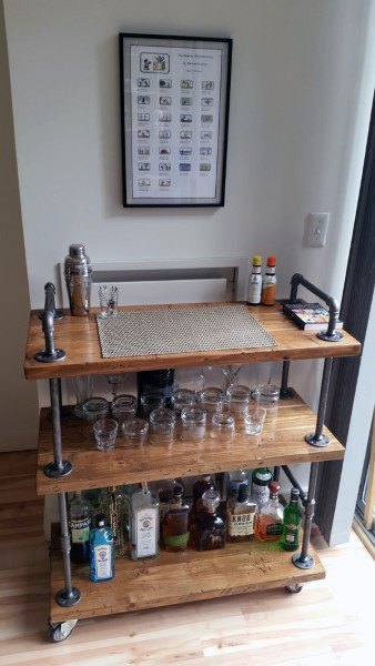 Industrial bar cart with wood shelves, steel pipe frame, glassware, and liquor bottle storage.