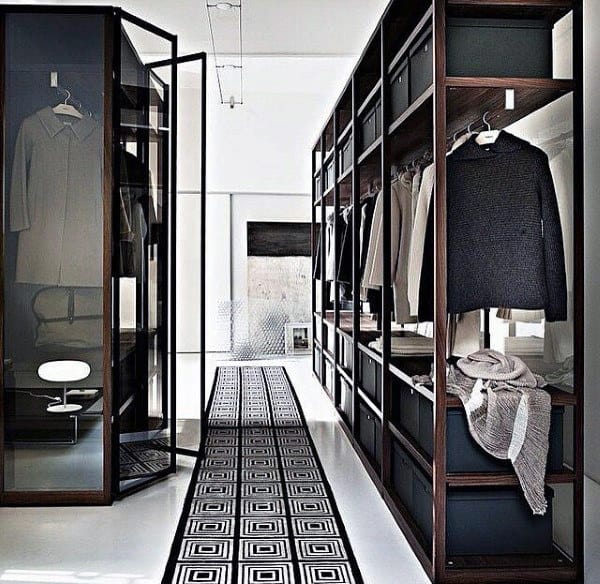 Modern walk-in closet with glass doors, organized shelves, hanging clothes, and geometric rug