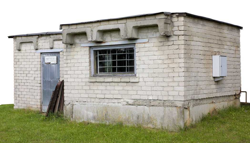 Simple backyard stone shed with a flat roof, metal door, and barred window.