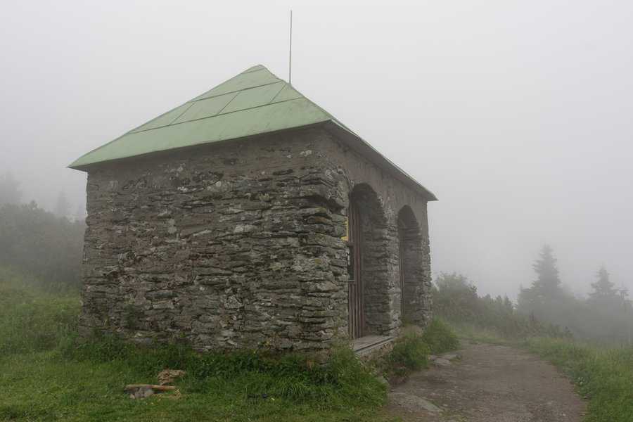 Stone shed with a green metal roof, set in a foggy and remote landscape.