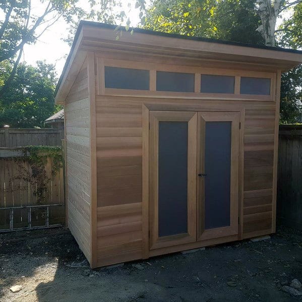 Simple wooden box-style shed with frosted glass windows and double doors in a backyard setting.