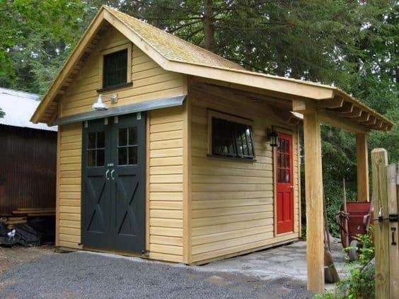 Rustic wooden shed with dark barn-style doors, a red side door, and a covered porch.