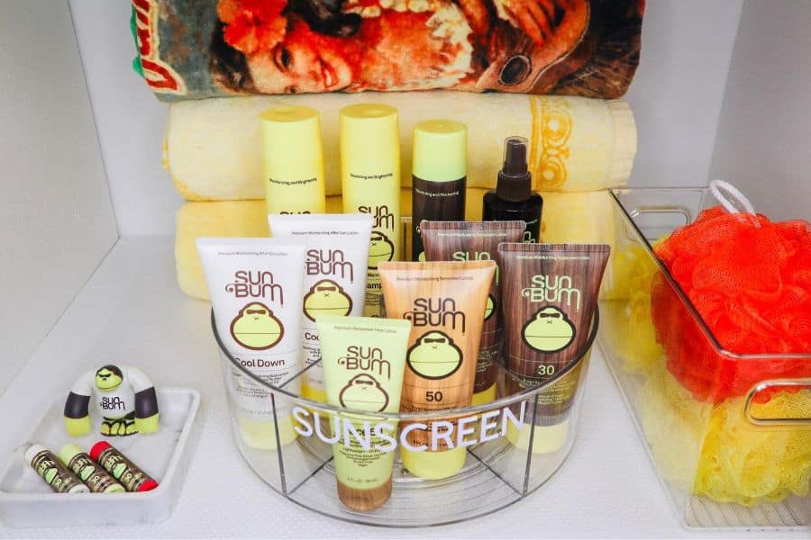 Sunscreen products neatly organized with towels and bath accessories in a bathroom storage setup.