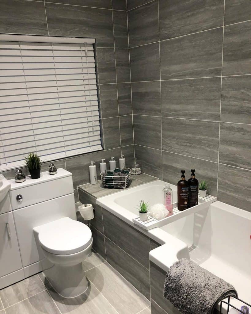 Small bathroom with grey slate tiles, white vanity, and a tub featuring bath accessories.