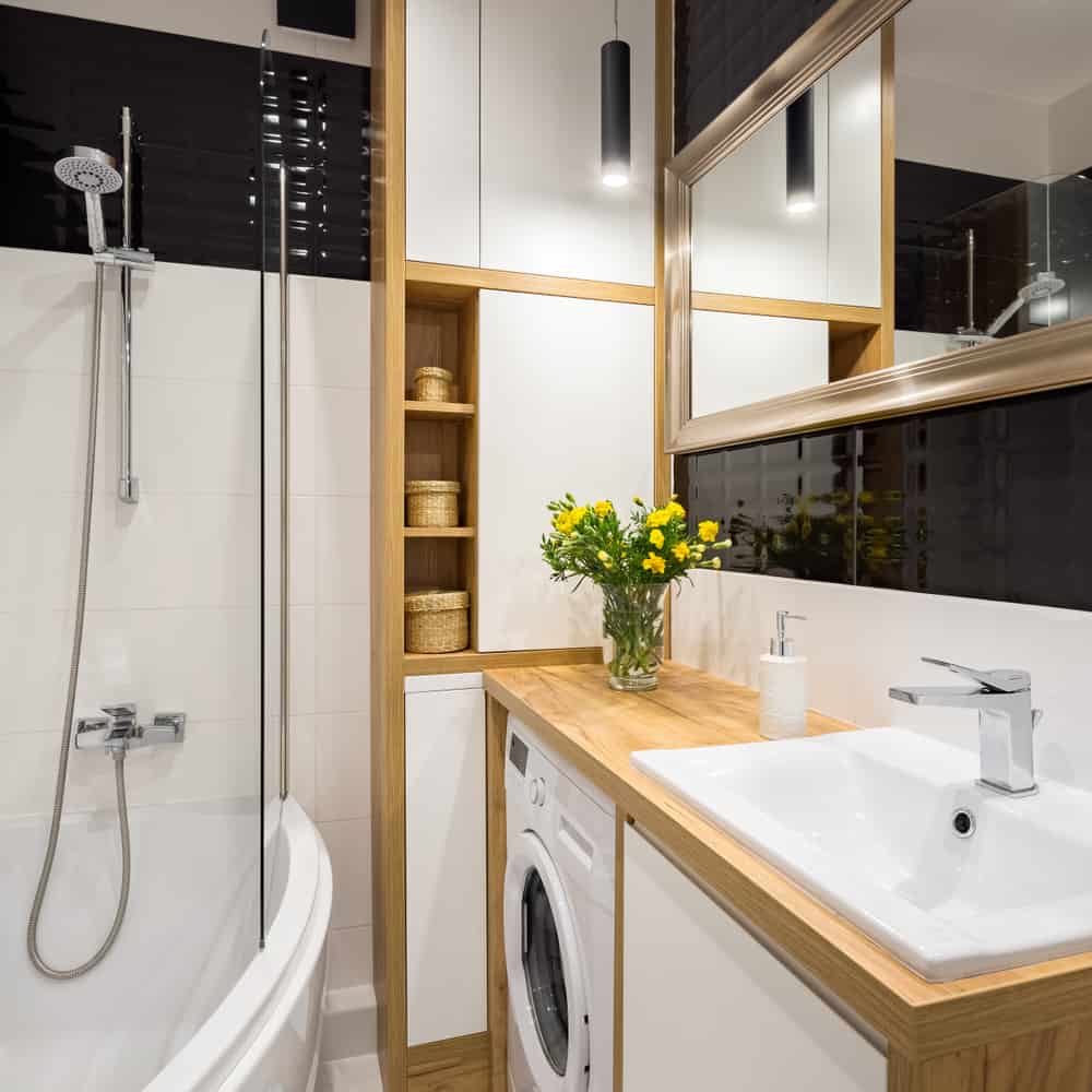 Small bathroom with wood accents, built-in storage, washer, white sink, and yellow flowers.